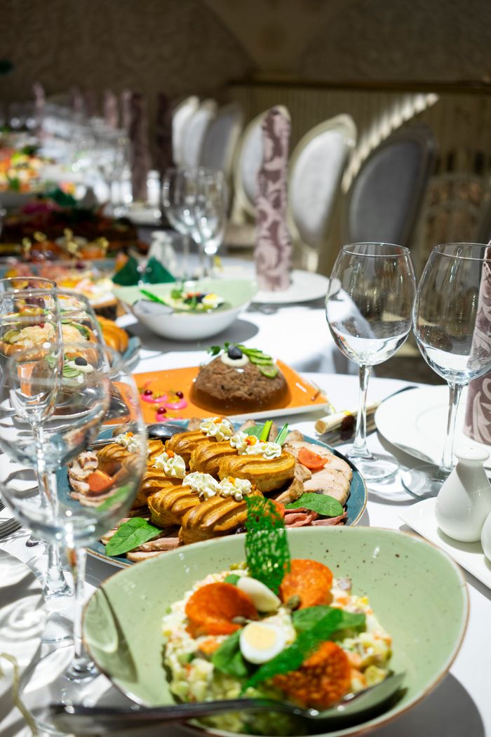 Served table with assorted food and dishes with cutlery and empty wineglasses on tablecloth near chairs in modern restaurant during dinner